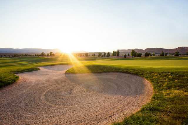 A sunny day view of a green protected by a manicured bunker at Sun River Golf Club.