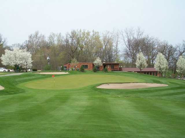 A view of green protected by sand traps and blooming trees at Cedar Creek Golf Course